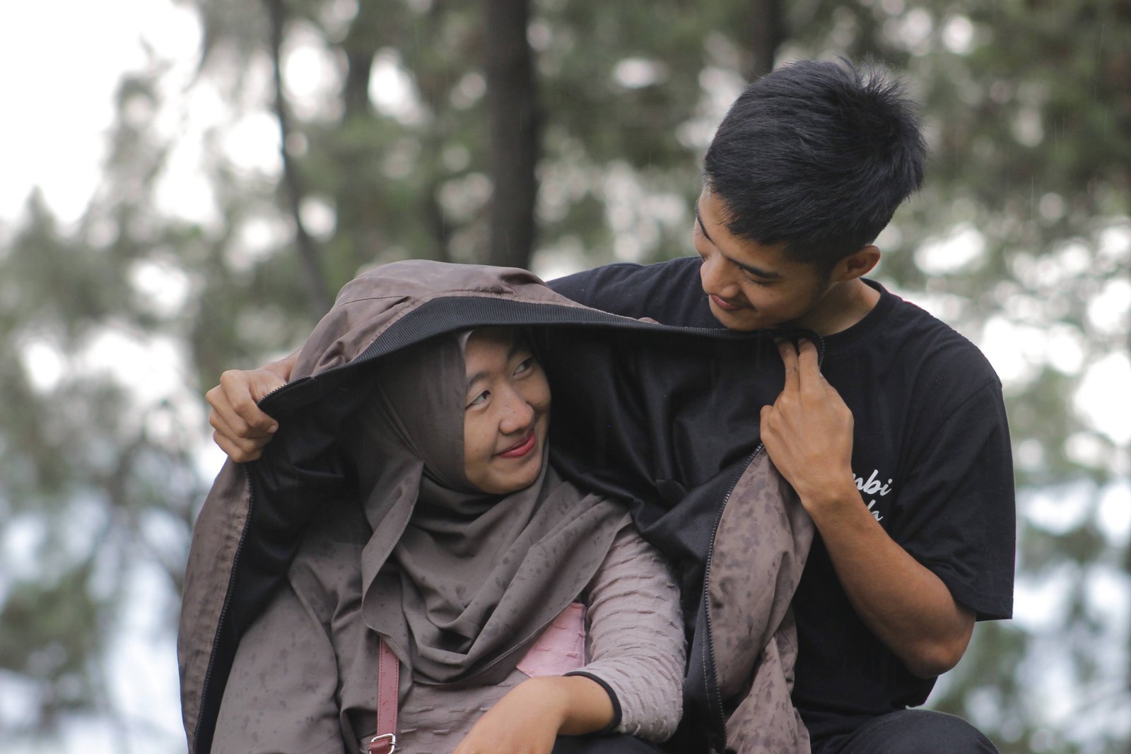 Two people sheltering under a jacket in the rain